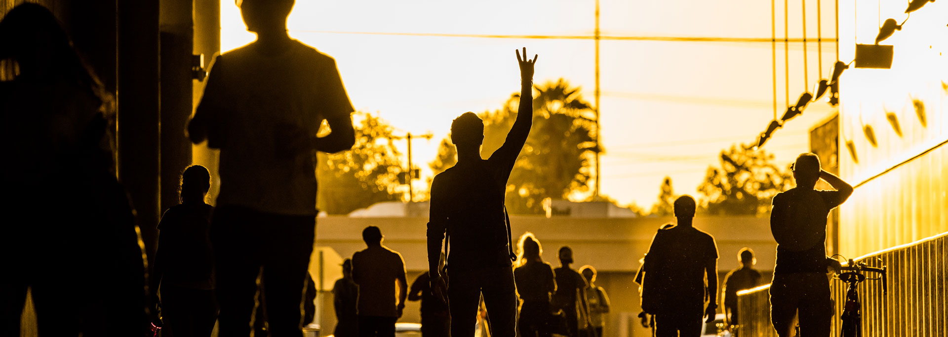 A silhouette of a person doing the pitchfork hand sign on campus.